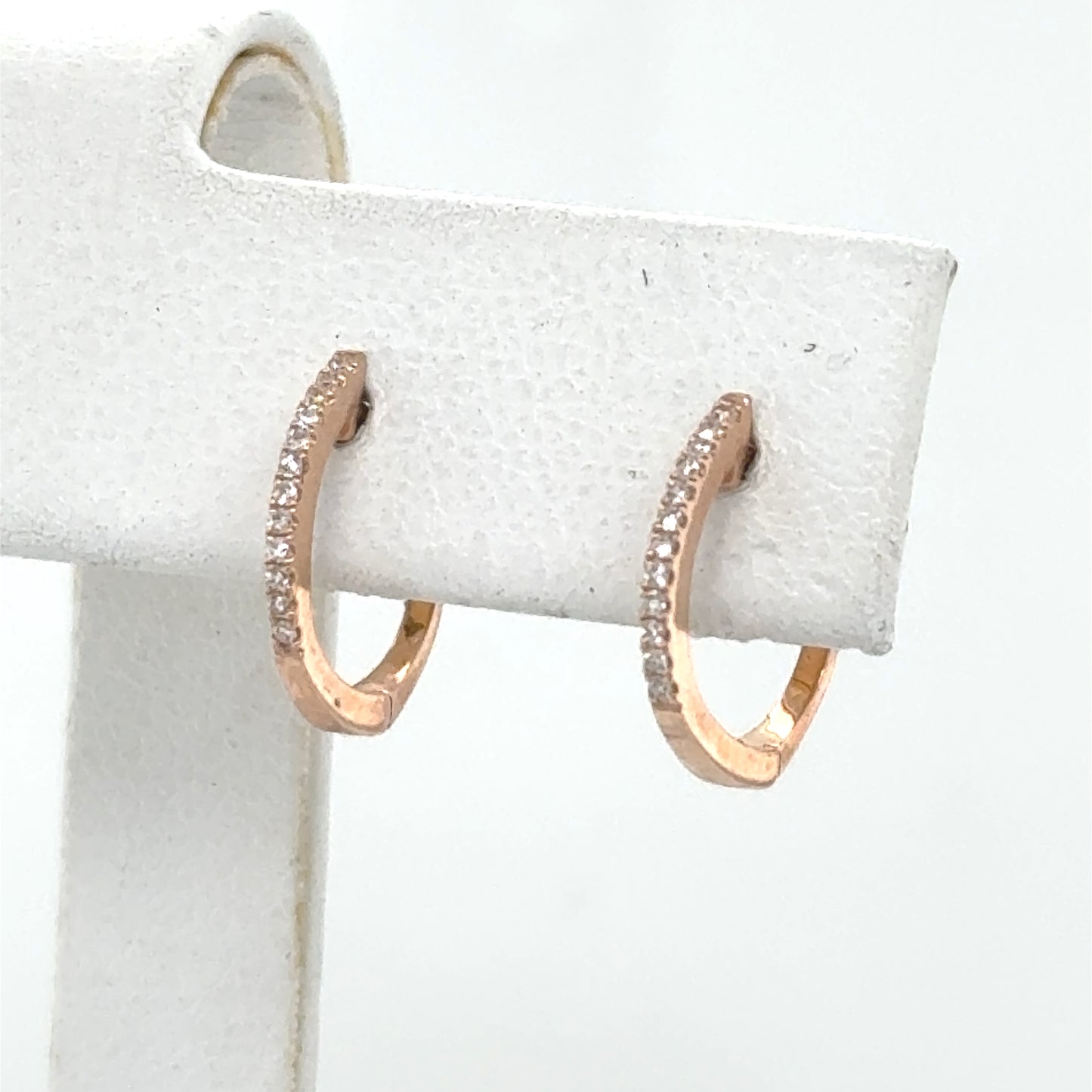 Small 14K rose gold huggie hoop earrings with a single diamond row.