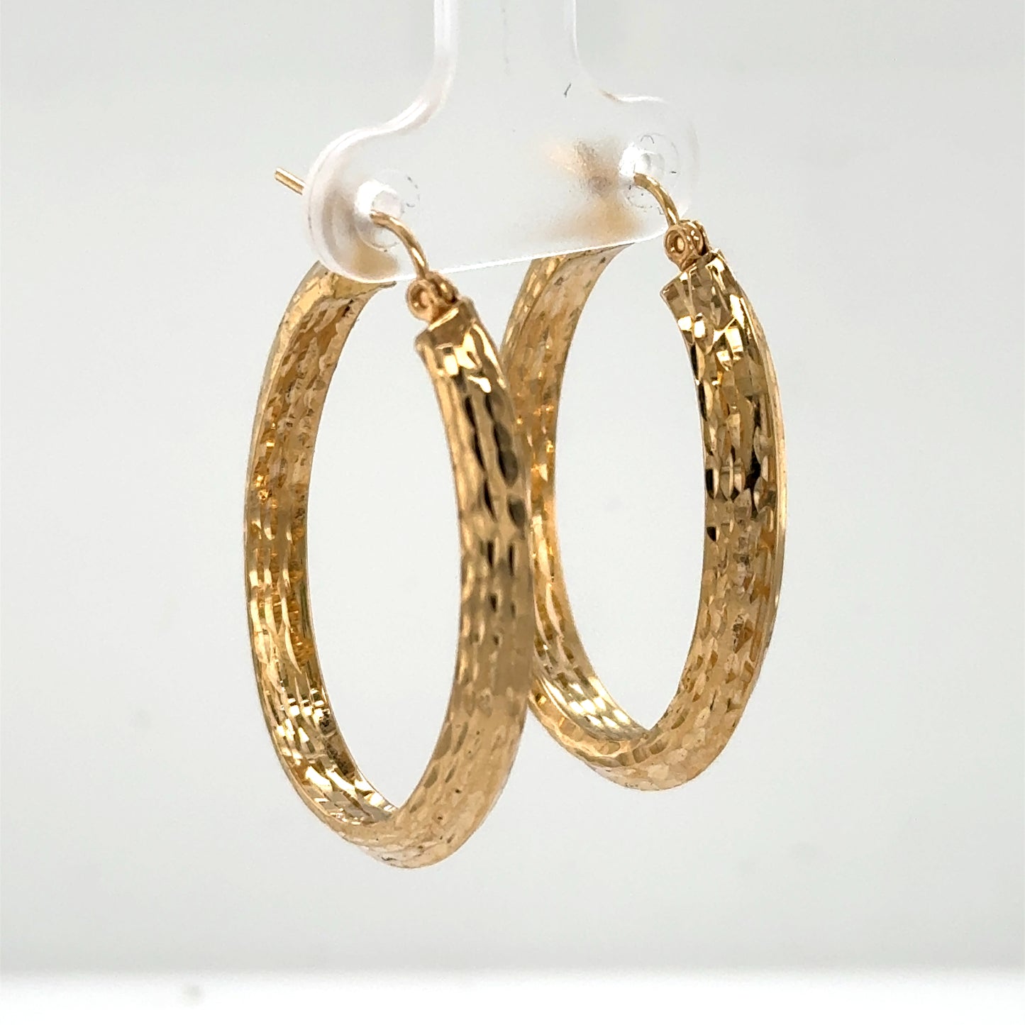 14K yellow gold oval hoop earrings with diamond-cut textured finish and hinged posts.