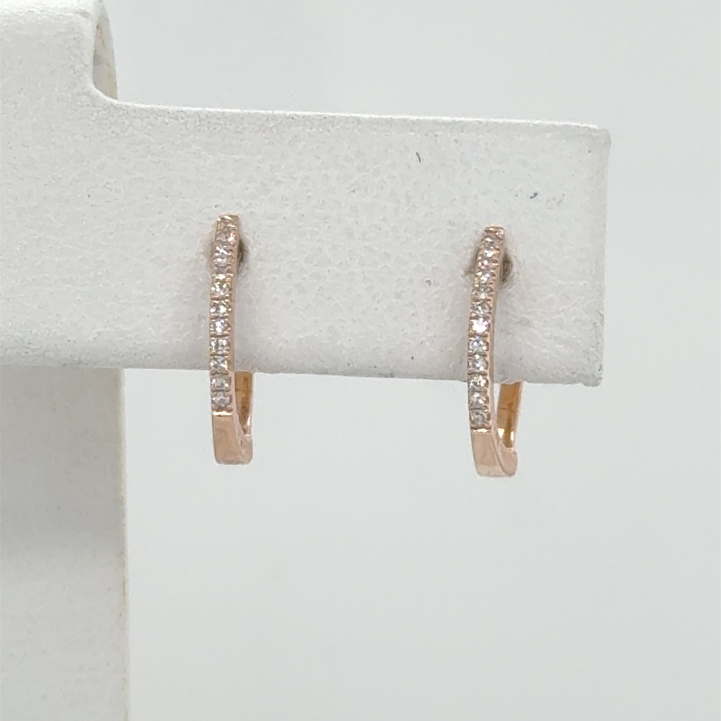 Small 14K rose gold huggie hoops with a front row of diamonds.