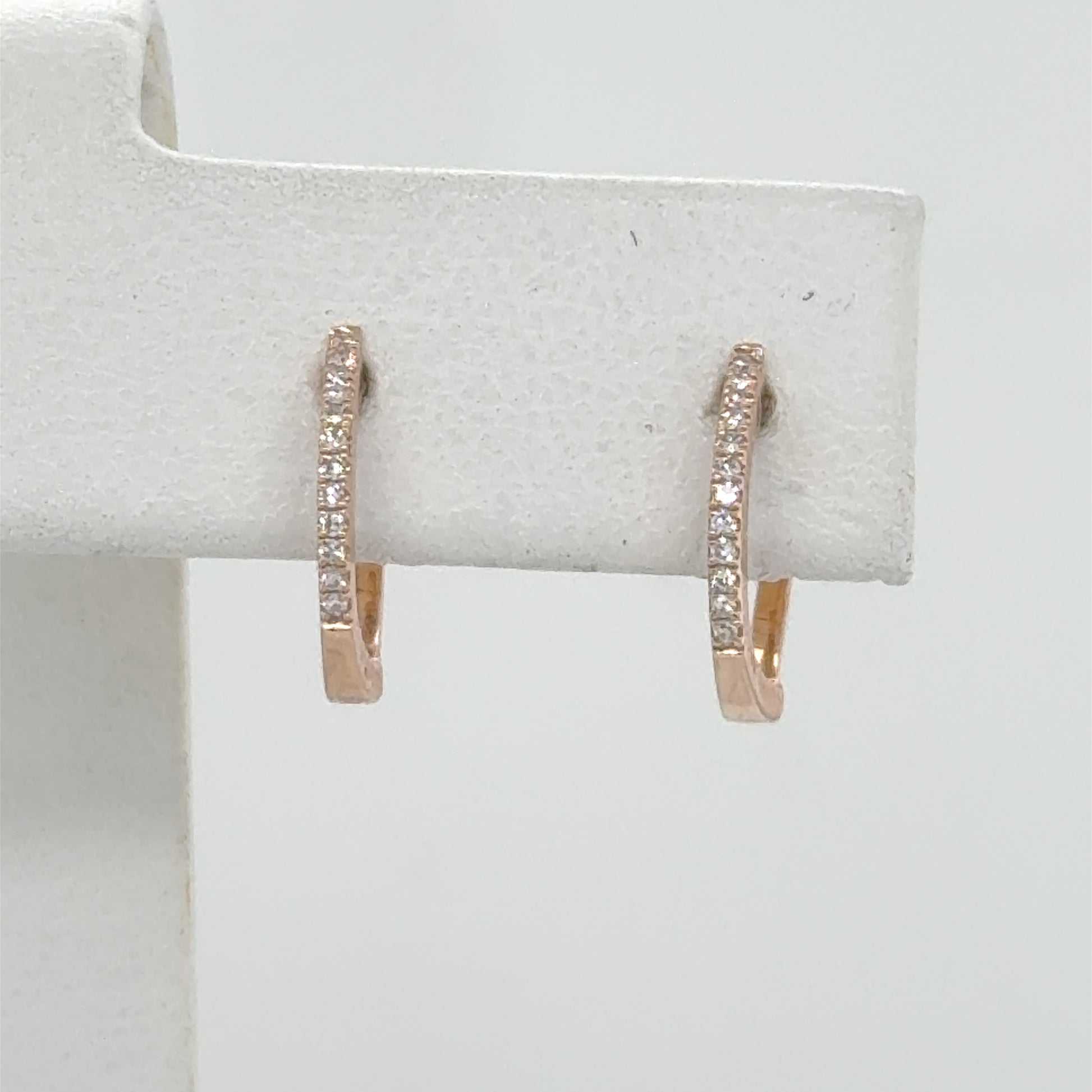 Small 14K rose gold huggie hoops with a front row of diamonds.