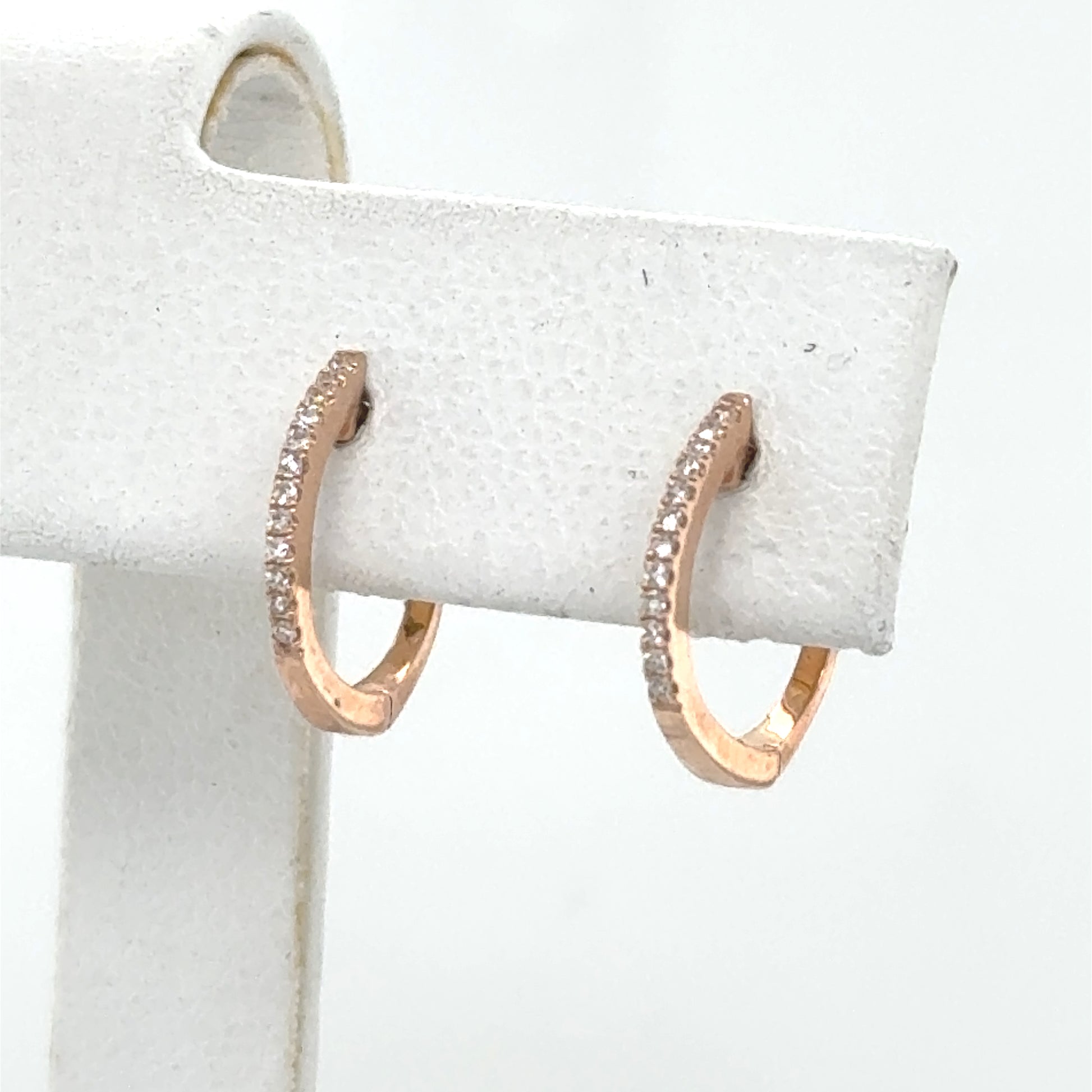 Small 14K rose gold huggie hoop earrings with a single diamond row.