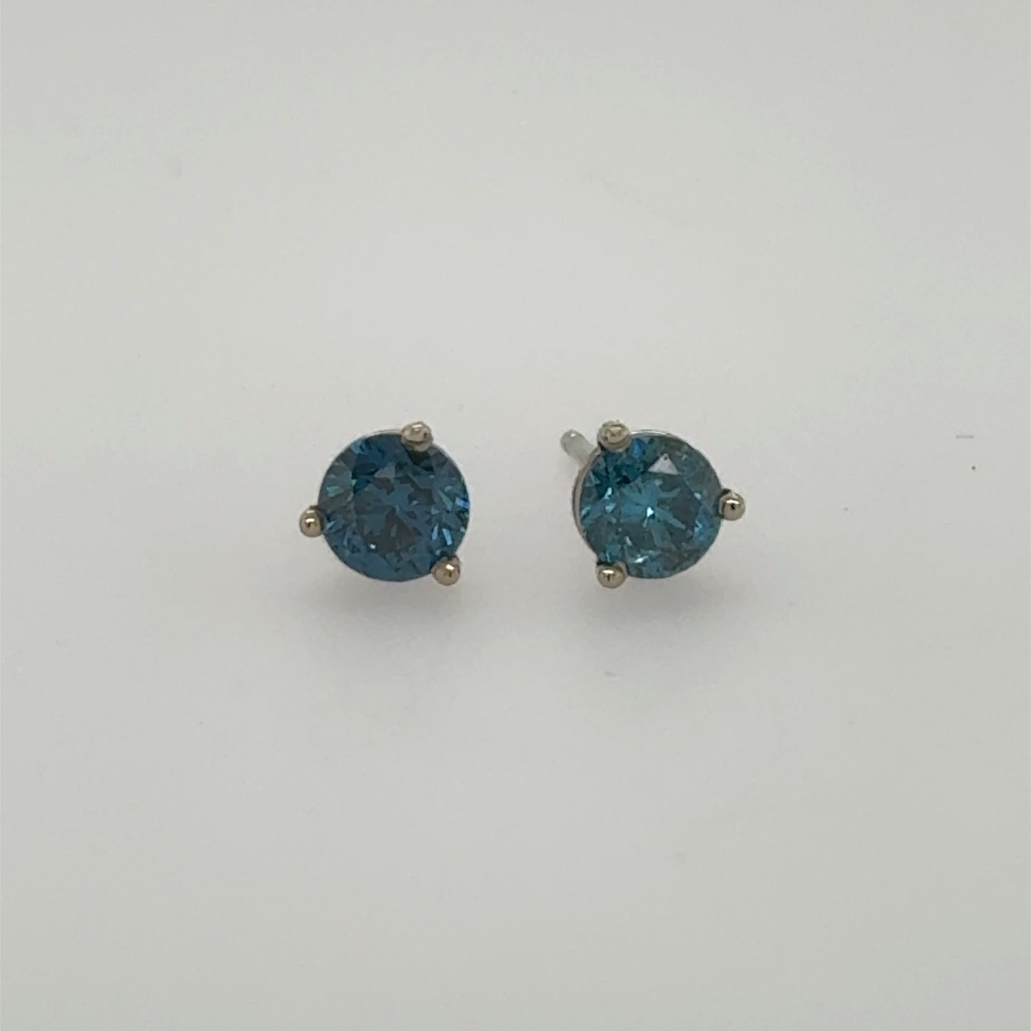 Round blue diamond stud earrings in 14K white gold three-prong settings.