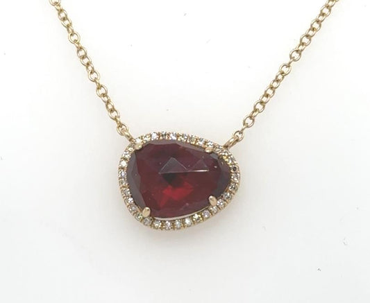 14K yellow gold necklace with asymmetrical red garnet pendant framed by diamond halo.