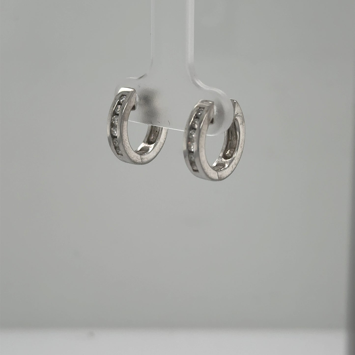 Small 14K white gold huggie hoops with channel‑set round diamonds.