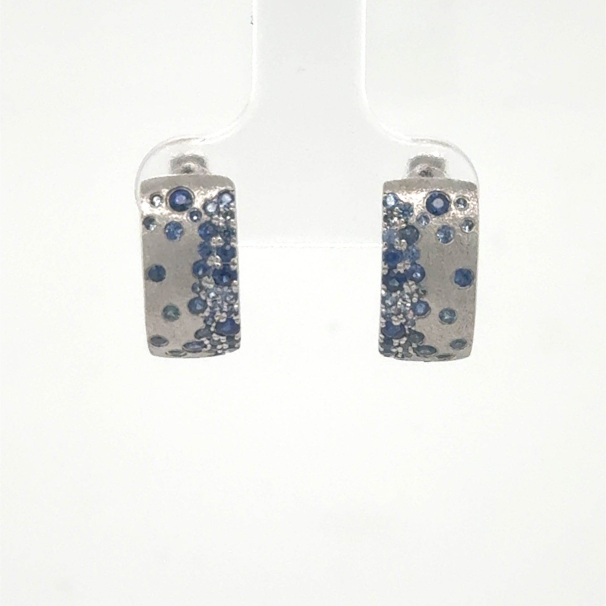 14K white gold huggie hoops with scattered blue sapphire pavé accents.