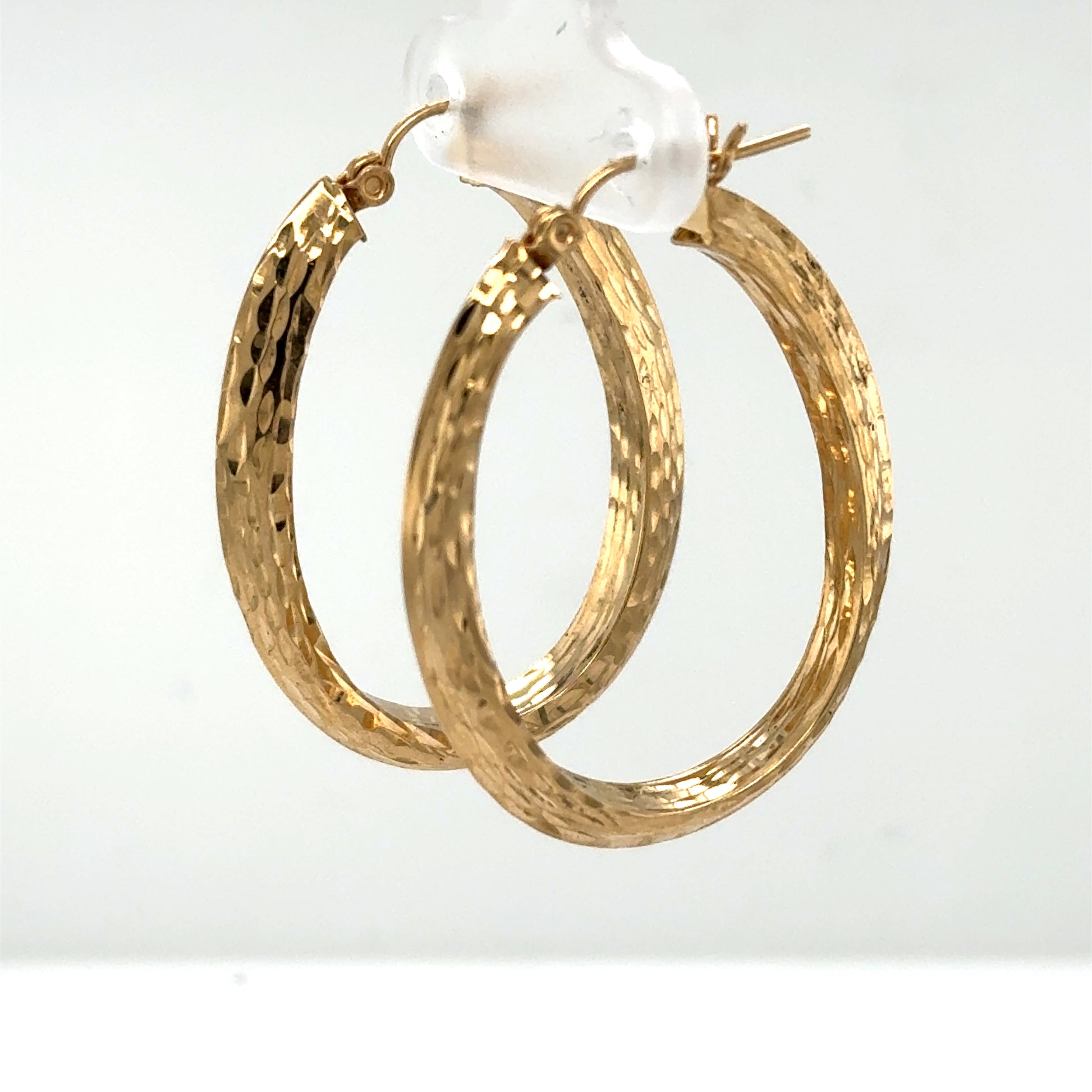14K yellow gold oval hoop earrings with diamond-cut texture and latch-back closures.