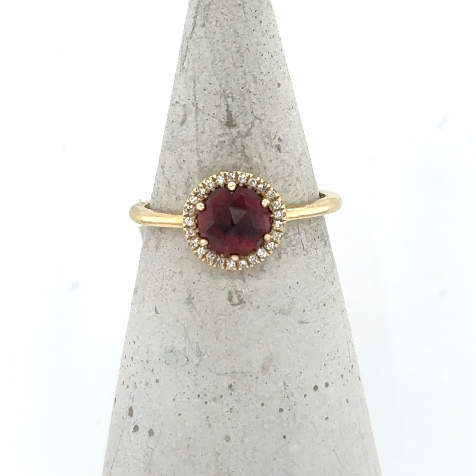 Yellow gold ring with round red garnet and diamond halo on slim band.