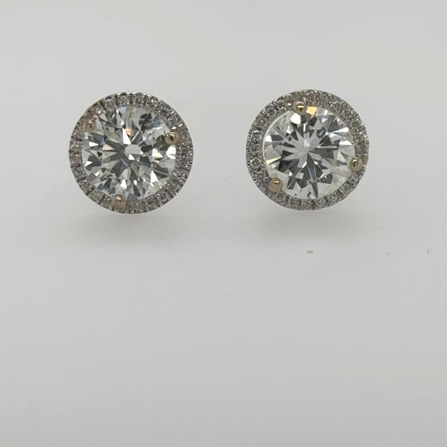 Round diamond stud earrings in white gold with halo and three-prong settings.