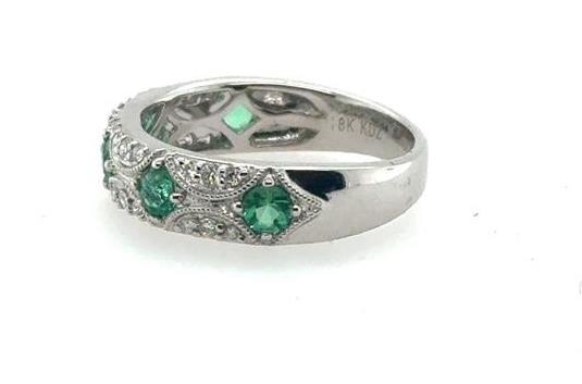 18K white gold band with round green emeralds and small diamond accents.