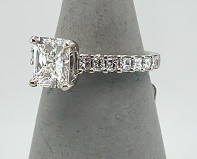 18K white gold ring with radiant-cut diamond in four prongs and princess-cut diamond band.
