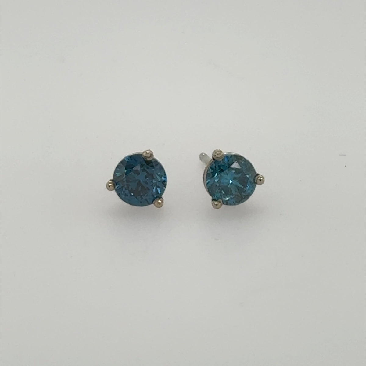 Round blue diamond stud earrings in 14K white gold three-prong settings.