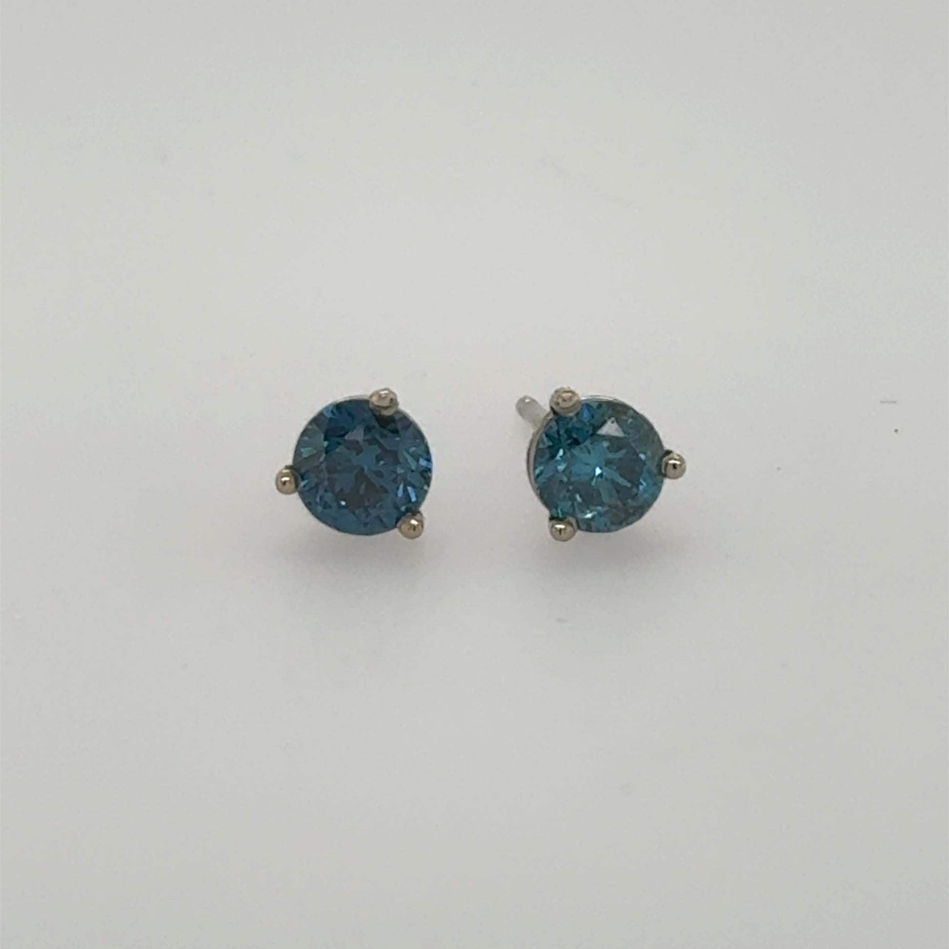 Round blue diamond stud earrings in 14K white gold three-prong settings.