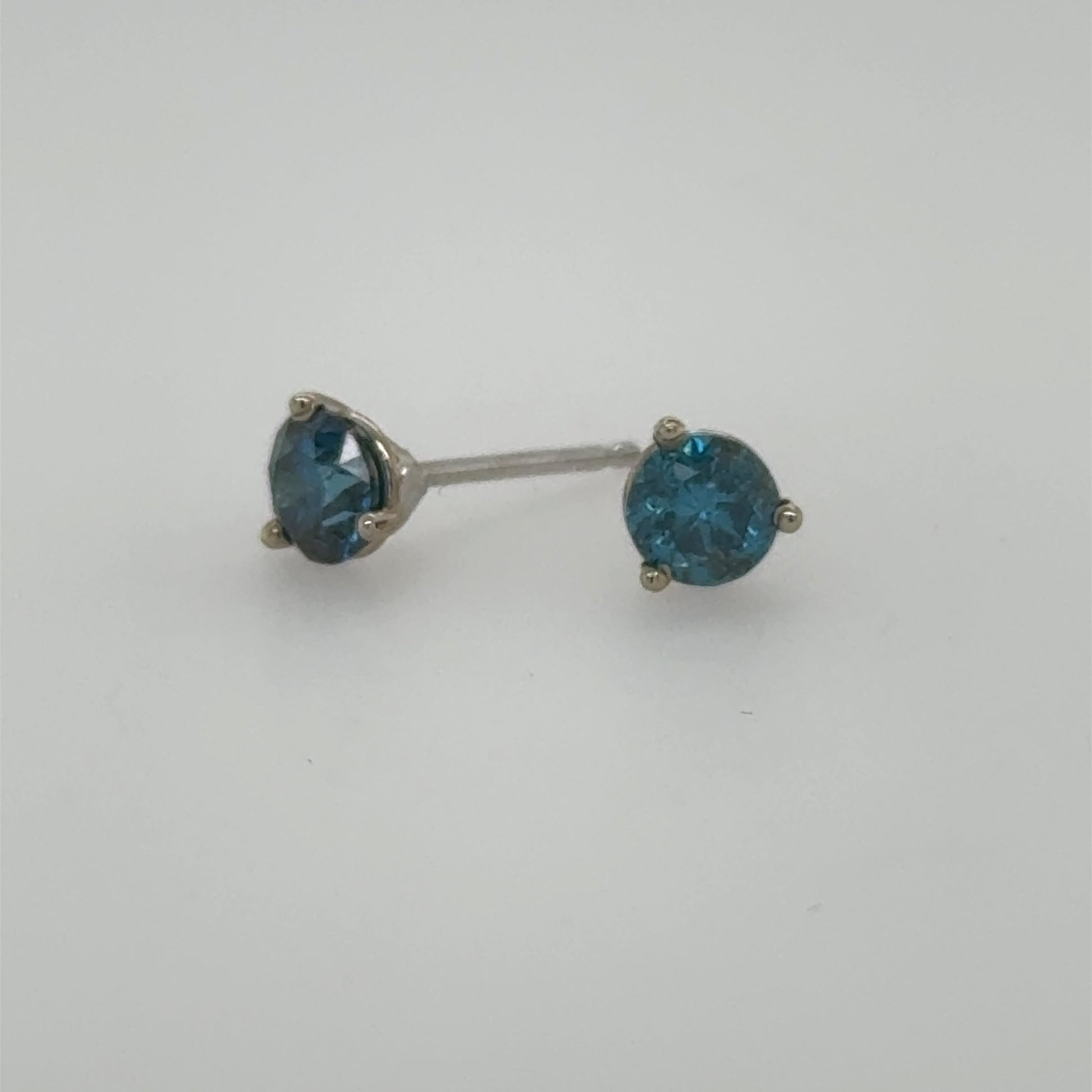 Blue round diamond stud earrings in 14K white gold three-prong settings.