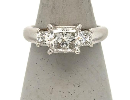 Platinum three-stone ring with princess-cut center diamond and two side diamonds.