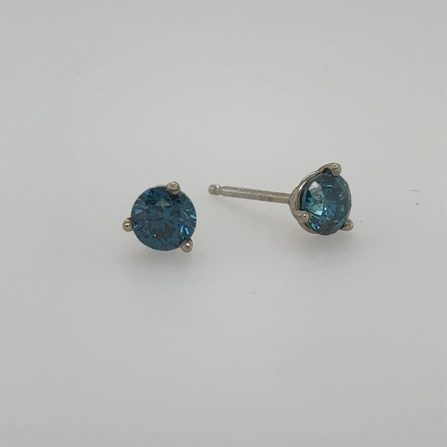 Blue round-cut diamond stud earrings in 14K white gold three-prong settings.