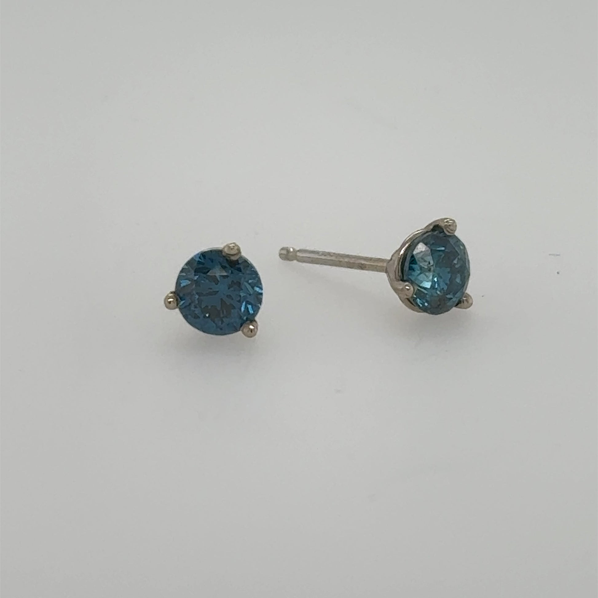 Blue round-cut diamond stud earrings in 14K white gold three-prong settings.