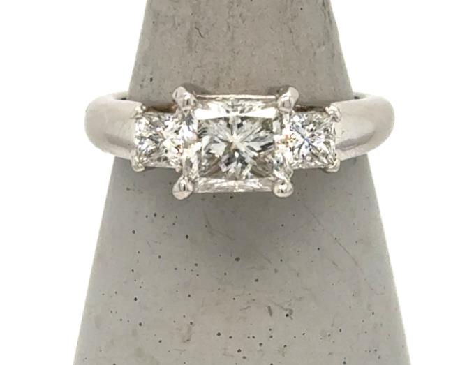 Platinum three-stone ring with princess-cut center diamond and two side diamonds.
